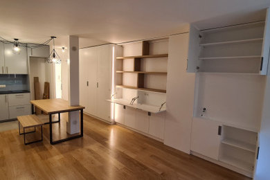 Cette photo montre une grande salle de séjour tendance ouverte avec une bibliothèque ou un coin lecture, un mur blanc, parquet clair et un téléviseur dissimulé.
