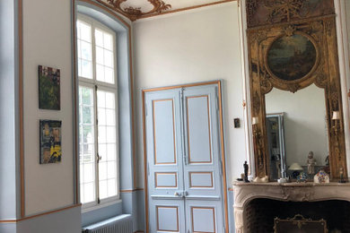 Cette photo montre un grand salon chic avec un mur bleu, parquet clair, une cheminée standard, un manteau de cheminée en bois, un plafond voûté, boiseries et un plafond cathédrale.