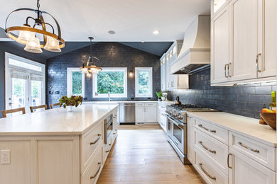 This is an example of a large traditional u-shaped separate kitchen in DC Metro with recessed-panel cabinets, light wood cabinets, marble benchtops, black splashback, subway tile splashback, panelled appliances, light hardwood floors, with island, beige floor and white benchtop.