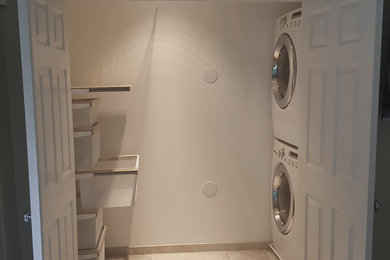 Laundry closet - mid-sized contemporary ceramic tile laundry closet idea in Boston with open cabinets, light wood cabinets, white walls and a stacked washer/dryer