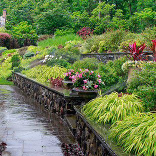 Large victorian backyard full sun formal garden in New York with a retaining wall and concrete pavers for winter.