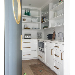 Idéer för att renovera ett maritimt vit vitt skafferi, med en undermonterad diskho, skåp i shakerstil, vita skåp, vitt stänkskydd, rostfria vitvaror, ljust trägolv och beiget golv