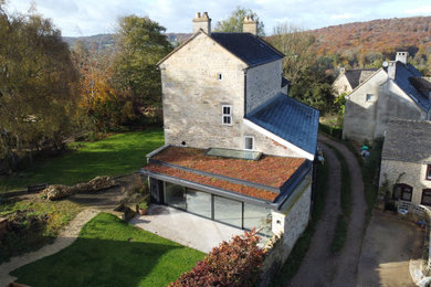 Photo of a contemporary bungalow house exterior in Gloucestershire with stone cladding, a flat roof and a green roof.