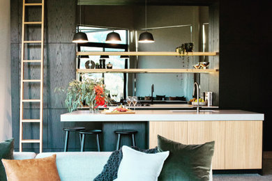 Design ideas for a large contemporary l-shaped open plan kitchen in Melbourne with concrete floors, grey floor, timber, a double-bowl sink, solid surface benchtops, mirror splashback, black appliances, with island, grey benchtop, raised-panel cabinets, black cabinets and metallic splashback.