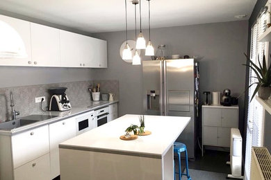 Large industrial galley separate kitchen in Paris with a single-bowl sink, flat-panel cabinets, white cabinets, laminate benchtops, grey splashback, stainless steel appliances, painted wood floors, with island, grey floor and white benchtop.