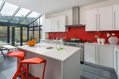 Photo of a mid-sized contemporary l-shaped open plan kitchen in London with an undermount sink, flat-panel cabinets, grey cabinets, red splashback, glass sheet splashback, stainless steel appliances, porcelain floors and with island.
