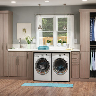 Inspiration for a medium sized industrial single-wall separated utility room in New York with a built-in sink, flat-panel cabinets, a side by side washer and dryer, grey walls, light hardwood flooring and grey cabinets.