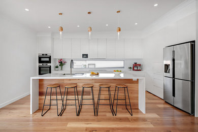 This is an example of a large modern l-shaped kitchen in Sydney with an undermount sink, flat-panel cabinets, white cabinets, quartz benchtops, white splashback, glass sheet splashback, stainless steel appliances, with island, brown floor, white benchtop and medium hardwood floors.