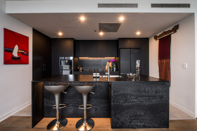 Design ideas for a mid-sized contemporary galley open plan kitchen in Sydney with an undermount sink, flat-panel cabinets, black cabinets, quartz benchtops, black splashback, engineered quartz splashback, black appliances, medium hardwood floors, with island and black benchtop.