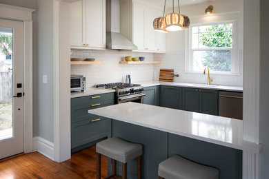Inspiration for a mid-sized arts and crafts u-shaped kitchen in Portland with an undermount sink, raised-panel cabinets, blue cabinets, quartz benchtops, white splashback, ceramic splashback, stainless steel appliances, light hardwood floors, with island and white benchtop.
