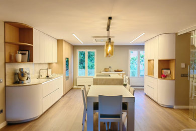 Example of a mid-sized minimalist medium tone wood floor open concept kitchen design in Madrid with recessed-panel cabinets, white cabinets, marble countertops, beige backsplash, marble backsplash, an island and beige countertops