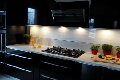 Photo of a mid-sized contemporary single-wall eat-in kitchen in Paris with an undermount sink, beaded inset cabinets, black cabinets, quartzite benchtops, white splashback, ceramic splashback, black appliances, ceramic floors, with island, grey floor and white benchtop.
