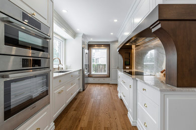 Example of a mid-sized classic u-shaped light wood floor and brown floor eat-in kitchen design in Montreal with an undermount sink, raised-panel cabinets, white cabinets, granite countertops, beige backsplash, granite backsplash, stainless steel appliances, an island and beige countertops