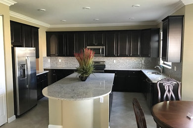 Mid-sized elegant u-shaped gray floor eat-in kitchen photo in Miami with a double-bowl sink, raised-panel cabinets, black cabinets, granite countertops, multicolored backsplash, mosaic tile backsplash, stainless steel appliances, an island and gray countertops