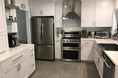 Photo of a small transitional eat-in kitchen in Los Angeles with a farmhouse sink, recessed-panel cabinets, white cabinets, grey splashback, stainless steel appliances, with island and grey floor.