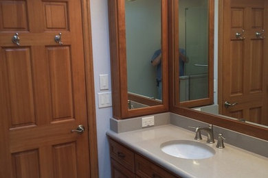 Example of a small trendy 3/4 beige tile and ceramic tile porcelain tile bathroom design in Portland with louvered cabinets, medium tone wood cabinets, solid surface countertops, a two-piece toilet, white walls and an undermount sink