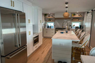 Inspiration for a mid-sized cottage l-shaped vinyl floor and brown floor kitchen remodel in New York with a farmhouse sink, shaker cabinets, white cabinets, quartz countertops, white backsplash, subway tile backsplash, stainless steel appliances, an island and white countertops