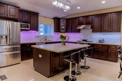 Trendy l-shaped porcelain tile and beige floor open concept kitchen photo in San Francisco with raised-panel cabinets, dark wood cabinets, quartzite countertops, white backsplash, an island and stainless steel appliances
