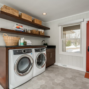 Diseño de lavadero lineal, retro, de tamaño medio, con fregadero bajoencimera, puertas de armario de madera en tonos medios, encimera de granito, paredes grises, suelo de baldosas de cerámica, lavadora y secadora juntas, suelo gris, encimeras negras y armarios abiertos