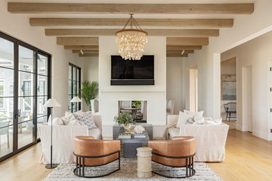 Beach style open concept light wood floor and exposed beam living room photo in Charleston with white walls, a two-sided fireplace, a plaster fireplace and a wall-mounted tv