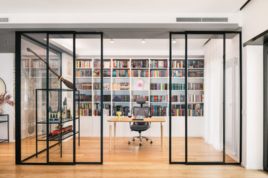 Immagine di un grande studio minimal con libreria, pareti bianche, parquet chiaro, scrivania autoportante e pavimento marrone
