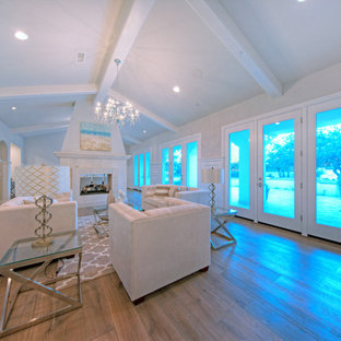 Modelo de salón para visitas abierto, mediterráneo, grande, con paredes beige, suelo de madera clara, chimenea de doble cara y marco de chimenea de piedra