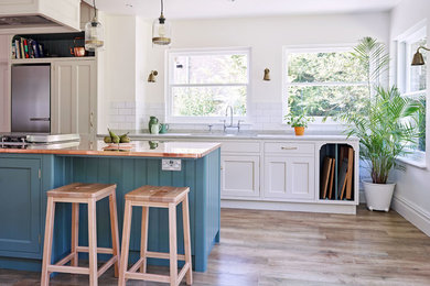 Design ideas for a large traditional l-shaped eat-in kitchen in London with blue cabinets, copper benchtops, white splashback, subway tile splashback, light hardwood floors and white benchtop.