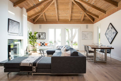 Example of a large trendy open concept medium tone wood floor living room design in Los Angeles with white walls, a standard fireplace, a stone fireplace and no tv