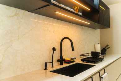 Inspiration for a medium sized cream and black single-wall open plan kitchen in London with beige cabinets, quartz worktops, beige splashback, engineered quartz splashback, black appliances, porcelain flooring, an island, grey floors, beige worktops and feature lighting.