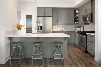 Inspiration for a transitional l-shaped kitchen in Edmonton with an undermount sink, recessed-panel cabinets, grey cabinets, grey splashback, subway tile splashback, stainless steel appliances, dark hardwood floors and a peninsula.
