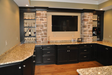 Mid-sized elegant u-shaped medium tone wood floor seated home bar photo in Baltimore with an undermount sink, recessed-panel cabinets, black cabinets and granite countertops