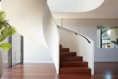 Mid-sized contemporary wood curved staircase in Melbourne with wood risers and metal railing.