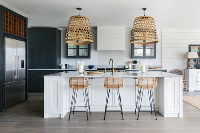 Inspiration for an expansive beach style open plan kitchen in London with glass-front cabinets, blue cabinets, stainless steel appliances, light hardwood floors, with island, grey benchtop and granite benchtops.