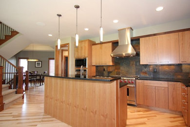 Kitchen - mid-sized traditional l-shaped light wood floor kitchen idea in Other with an undermount sink, flat-panel cabinets, light wood cabinets, soapstone countertops, black backsplash, stone tile backsplash, stainless steel appliances and an island