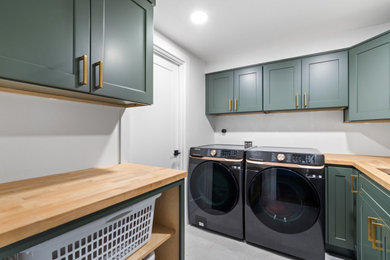 Mid-sized country porcelain tile and gray floor laundry room photo in Portland with an undermount sink, shaker cabinets, green cabinets, wood countertops, white walls, a side-by-side washer/dryer and brown countertops