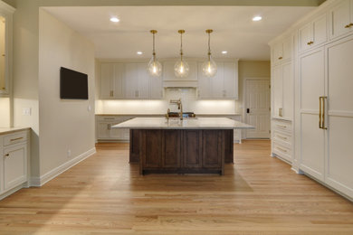 Example of a large transitional medium tone wood floor and brown floor kitchen design in Kansas City with beaded inset cabinets, white cabinets, quartzite countertops, white backsplash, subway tile backsplash, paneled appliances, an island, beige countertops and an undermount sink