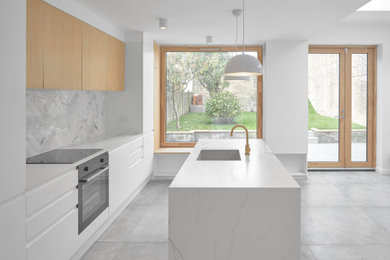 This is an example of a mid-sized industrial galley open plan kitchen in London with an undermount sink, flat-panel cabinets, medium wood cabinets, quartz benchtops, white splashback, ceramic splashback, coloured appliances, cement tiles, with island, grey floor and white benchtop.