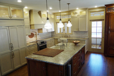 Eat-in kitchen - mid-sized traditional l-shaped medium tone wood floor and brown floor eat-in kitchen idea in Nashville with a farmhouse sink, shaker cabinets, granite countertops, multicolored backsplash, ceramic backsplash, paneled appliances, an island and multicolored countertops