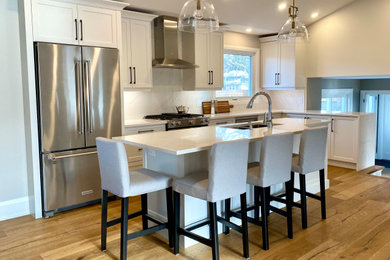 Example of a mid-sized country l-shaped medium tone wood floor and vaulted ceiling open concept kitchen design in Toronto with an undermount sink, shaker cabinets, white cabinets, quartz countertops, white backsplash, quartz backsplash, stainless steel appliances, an island and white countertops