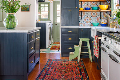 Example of a mid-sized eclectic galley medium tone wood floor eat-in kitchen design in Los Angeles with a farmhouse sink, shaker cabinets, blue cabinets, marble countertops, multicolored backsplash, porcelain backsplash, white appliances, an island and white countertops