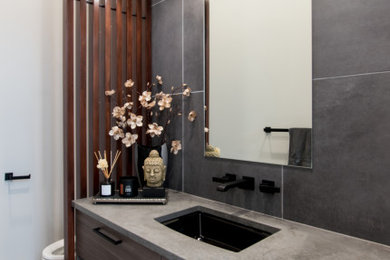 Mid-sized trendy gray tile and porcelain tile porcelain tile and black floor powder room photo in Seattle with flat-panel cabinets, brown cabinets, a wall-mount toilet, white walls, an undermount sink, quartz countertops, gray countertops and a floating vanity