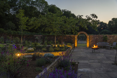 This is an example of a classic back formal garden in Sussex with a raised bed, natural stone paving and a stone fence.