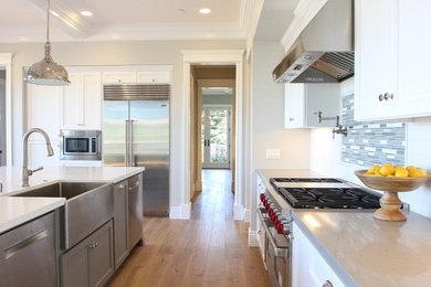 This is an example of a mid-sized transitional u-shaped eat-in kitchen in San Francisco with a farmhouse sink, white cabinets, quartzite benchtops, white splashback, ceramic splashback, stainless steel appliances, medium hardwood floors, with island and recessed-panel cabinets.