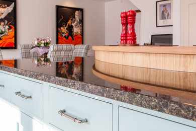 This is an example of a traditional u-shaped eat-in kitchen in West Midlands with flat-panel cabinets, blue cabinets, granite benchtops, light hardwood floors, with island, brown floor and multi-coloured benchtop.