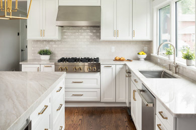 Example of a large classic medium tone wood floor kitchen design in New York with an undermount sink, shaker cabinets, quartzite countertops, beige backsplash, porcelain backsplash, stainless steel appliances and an island