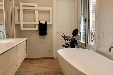 This is an example of a mid-sized contemporary master bathroom in Other with beaded inset cabinets, light wood cabinets, a freestanding tub, a curbless shower, a two-piece toilet, white tile, marble, grey walls, ceramic floors, a console sink, solid surface benchtops, an open shower and white benchtops.