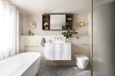 Photo of a small contemporary cream and black ensuite half tiled bathroom in London with flat-panel cabinets, white cabinets, a freestanding bath, a wall mounted toilet, beige tiles, ceramic tiles, beige walls, ceramic flooring, a submerged sink, marble worktops, grey floors, grey worktops, a single sink and a floating vanity unit.