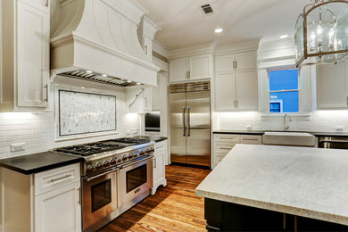 Large arts and crafts medium tone wood floor and brown floor eat-in kitchen photo in Houston with a farmhouse sink, shaker cabinets, white cabinets, marble countertops, white backsplash, cement tile backsplash, stainless steel appliances and an island