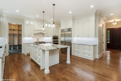 Inspiration for a large transitional u-shaped medium tone wood floor enclosed kitchen remodel in Chicago with an undermount sink, shaker cabinets, white cabinets, granite countertops, white backsplash, marble backsplash, stainless steel appliances and an island