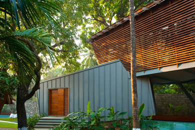 Design ideas for a tropical two-storey grey exterior in Mumbai with wood siding and a shed roof.